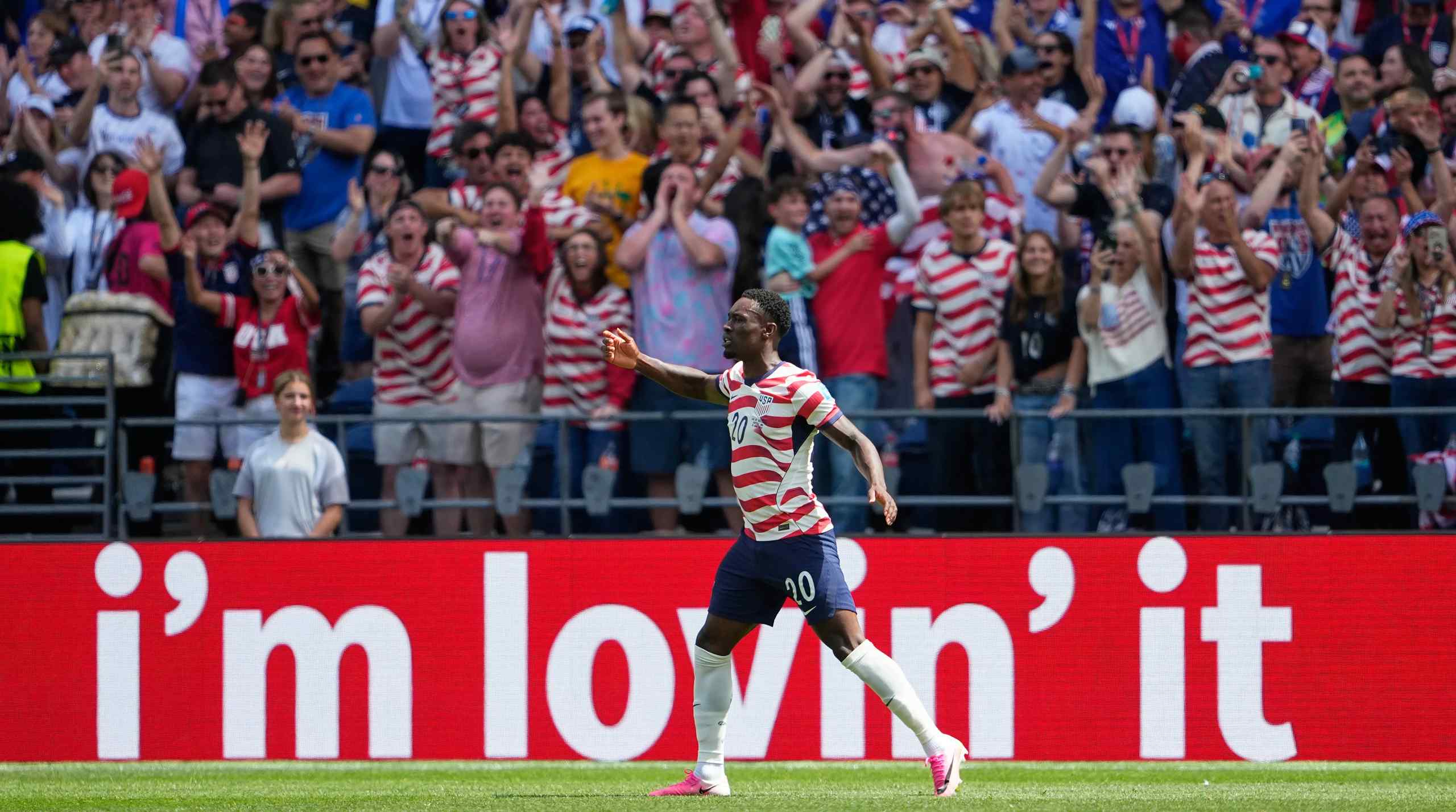 The USMNT's Flo Balogun on the soccer field with a McDonalds slogan on a billboard behind him.